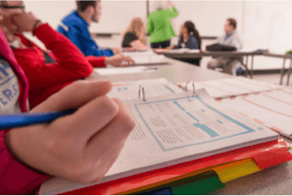 A student, studying in a classroom with an open notebook on the table.