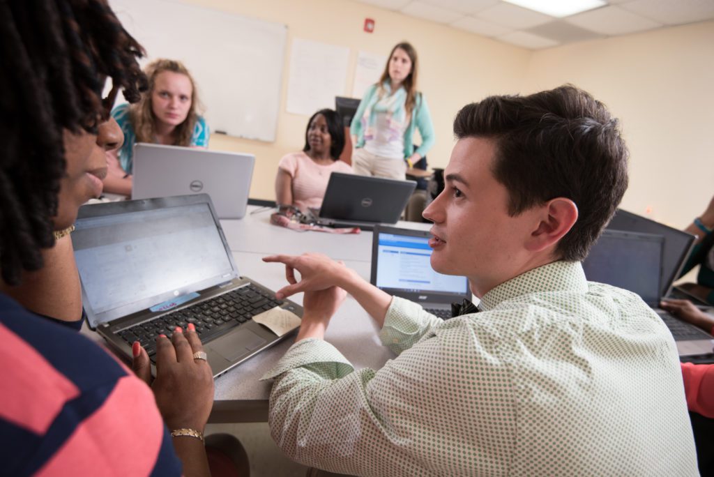 Graduate students sit in a classroom, working on a laptop. 