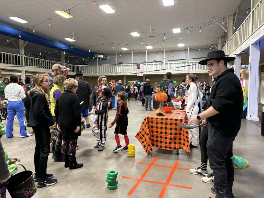 Student plays a game of tic tac toe with a family at Harvest Fest