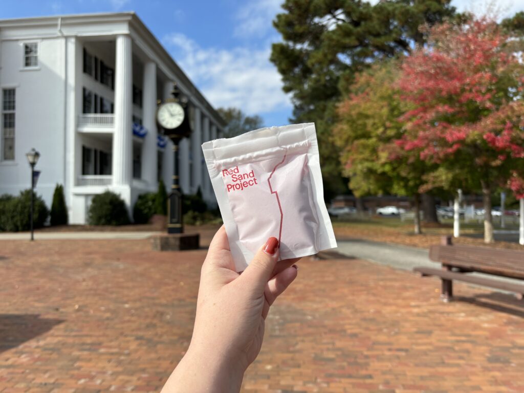 Hand holding a bad of sand for the Red Sand Project